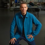 A man with a blue jacket looks at the camera in an art studio.